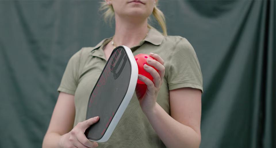 A person holding a pickleball racket and ball