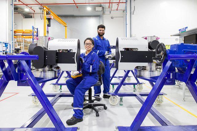 Two employees smiling at the camera. Each working on a piece of equipment