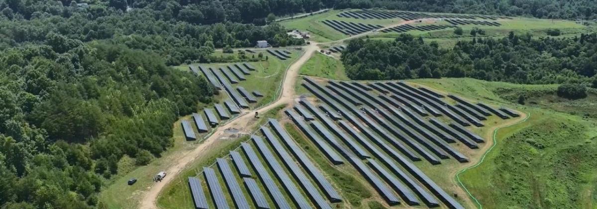Aerial view of fields of rows of solar panels in a forested area.