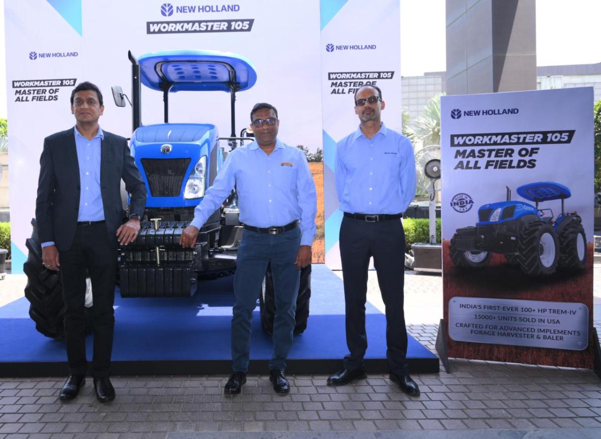 Three people standing next to a blue tractor on display.