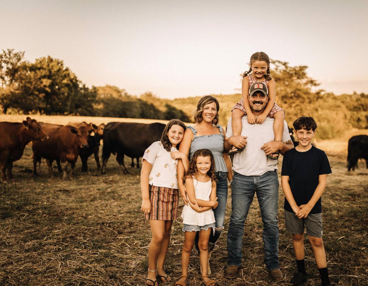 A family posed standing in a field in front of cows.