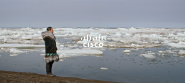 A person in warm clothing standing on a shore looking out over open water with chunks of ice and snow floating in it. "Cisco" overlaid.