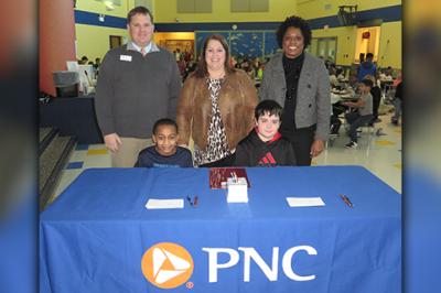 Fifth grade students at Eastside Elementary School in Anderson get ready to serve as student tellers for the launch of Indiana’s first PNC School Bank (Back row L to R): Chris Spolyar, PNC branch manager Anderson; Dr. Val Scott, principal Eastside Elementary School; Pat Gamble-Moore, PNC community development banking manager (Sitting L to R): Fifth graders Brycen Carter and Nicholas Kestner.