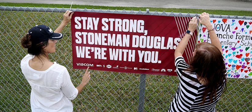 February 27, 2018 – Parkland, Florida, United States: Volunteers hang banners, including this one reading “Stay strong, Stoneman Douglas, we’re with you,” around the perimeter of Marjory Stoneman Douglas high school to welcome back students who returned to school on Feb. 28, two weeks after the mass shooting that killed 17 students and staff. (Susan Stocker/SF Sun Sentinel/Polaris)