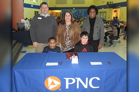 Fifth grade students at Eastside Elementary School in Anderson get ready to serve as student tellers for the launch of Indiana’s first PNC School Bank (Back row L to R): Chris Spolyar, PNC branch manager Anderson; Dr. Val Scott, principal Eastside Elementary School; Pat Gamble-Moore, PNC community development banking manager (Sitting L to R): Fifth graders Brycen Carter and Nicholas Kestner.